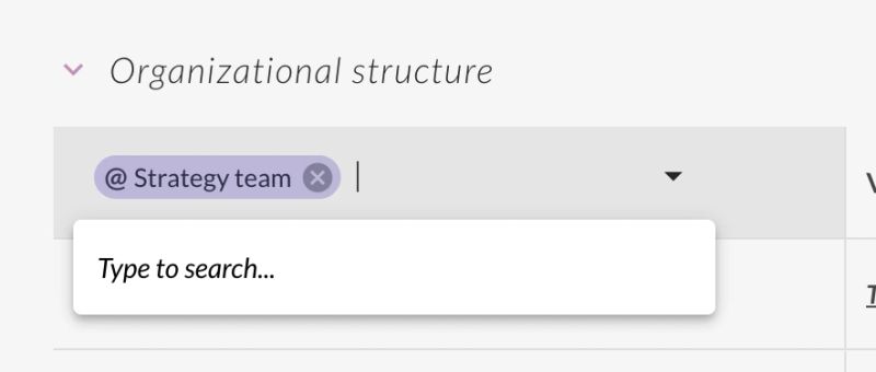 A tight crop of the Analytics app's "Organizational structure" search field, which is the control this step turns on. One filter chip sits in the field — "@ Strategy team", with an x for clearing it — next to a caret that opens the picker, and the dropdown below is already open and reading "Type to search…". So the scope of the whole Analytics table is set from this one field: type any workspace, reporting line or individual into it and swap it for the current selection. Only the left edge of the metric columns is visible at the right.